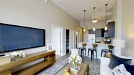 Located at 3 Sundial in Manchester, New Hampshire, this single-floor residence offers a thoughtfully designed open-concept layout that seamlessly connects the living, dining, and kitchen areas. Soaring ceilings lend an airy, expansive feel to the main living space, which is enhanced by neutral wall tones and contemporary finishes throughout.

The living area provides a comfortable and inviting atmosphere, featuring wall-mounted media accommodations, stylish area rugs, and ample room for furnishings. A large walk-in closet or storage space is conveniently accessible from the main living area, offering excellent organizational capacity.

The kitchen is a standout feature, outfitted with dark cabinetry, modern pendant lighting, a white refrigerator, and a breakfast bar with bar seating — ideal for casual dining and entertaining. The kitchen flows naturally into the living space, making it well-suited for social gatherings.

Track lighting runs along the ceiling, providing flexible and functional illumination across the open floor plan. The consistent use of dark hardwood-style flooring ties the spaces together cohesively. The overall design aesthetic balances modern sophistication with everyday practicality, creating a welcoming and functional home environment.