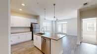 Located at 111 Grove Park Dr in Mooresville, NC, this thoughtfully designed 2-bedroom, 1-bathroom residence offers a clean, modern aesthetic across a single floor. The open-concept kitchen and living area serves as the heart of the home, anchored by a central island with a quartz-style countertop, an integrated sink, and elegant pendant lighting overhead. White shaker cabinetry, a classic subway tile backsplash, and a full suite of stainless steel appliances — including a refrigerator, range, microwave, and dishwasher — complete the well-appointed kitchen. Light wood-look flooring flows throughout the main living areas, enhancing the bright, airy atmosphere. The living room benefits from natural light streaming through French doors and multiple windows fitted with blinds, while a ceiling fan adds comfort. The primary bedroom offers a comfortable footprint and features plush carpeting and a walk-in closet with wire shelving for organized storage. The second bedroom also includes wood-look flooring and a bright window with outdoor views. The bathroom is finished with a gray-tone vanity countertop and wood-look flooring. A dedicated laundry room with a full-size washer and dryer rounds out this well-equipped, move-in-ready home.