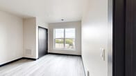 Located at 100 E National Ave in Milwaukee's vibrant Walker's Point neighborhood, this thoughtfully designed two-bedroom, two-bathroom unit offers a clean, contemporary aesthetic throughout. Light wood-tone flooring runs consistently across the single floor, complementing the neutral walls and dark accent trim that frame each room.

The kitchen serves as a functional centerpiece, featuring light maple cabinetry, dark countertops, a full suite of stainless steel appliances, and a central island with pendant lighting overhead — ideal for both meal prep and casual dining. The layout flows naturally toward the bedrooms, accessed through dark-paneled doors that add a modern contrast to the bright interior.

The primary bedroom is generously sized, boasting corner windows that frame sweeping views of the Milwaukee skyline and the Hoan Bridge, flooding the room with natural light. The second bedroom is more intimate, with its own window offering additional city views. Both bedrooms are served by two well-appointed bathrooms featuring light maple vanities with white countertops and tile flooring. One bathroom includes accessibility grab bars. Storage is addressed with two closets, including a walk-in fitted with wire shelving systems for organized storage.