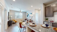 Allora New Forest presents a thoughtfully designed 2-bedroom, 2-bathroom residence located in Houston, TX 77049. The single-floor layout flows seamlessly from the kitchen through the dining area and into the living room, creating an open and connected living environment. The kitchen is equipped with stainless steel appliances, dark espresso cabinetry, a subway tile backsplash, granite countertops, and a central island that doubles as a breakfast bar — ideal for casual dining or meal prep. Light wood-style flooring runs consistently throughout the unit, enhancing the sense of continuity and warmth. The living area features recessed lighting, a ceiling fan, and a large window that invites natural light. Both bathrooms are finished with granite-topped vanities, dark cabinetry, and tiled tub-shower combinations. The primary bathroom includes a walk-in closet for added storage convenience. The bedrooms are generously proportioned, with neutral walls and windows offering views of surrounding greenery. Clean lines, neutral tones, and modern fixtures define the overall aesthetic, making this a well-appointed and functional living space suited for comfortable everyday living.