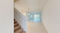 This well-designed two-story home offers a clean, contemporary aesthetic throughout, with a bright and airy atmosphere anchored by neutral tones and abundant natural light. The ground floor features an open, spacious living area finished with large-format tile flooring and a chandelier pendant that adds a refined touch to the entryway. Sliding glass doors with vertical blinds invite natural light and outdoor views into the main living space. The kitchen is a standout feature, showcasing crisp white shaker cabinetry, a large quartz-topped island with a double sink, stainless steel appliances including a refrigerator, range, and microwave, and stylish pendant lighting overhead. A dedicated laundry room on the ground floor includes built-in shelving for added convenience. Upstairs, the home provides four bedrooms, including a generously sized primary suite with a well-appointed en-suite bathroom featuring a dual-sink vanity with quartz countertops, a glass-enclosed walk-in shower, and tile flooring. The additional bedrooms are finished with soft carpet and multiple windows that frame leafy outdoor views. Two additional bathrooms serve the remaining bedrooms, one complete with a tub-shower combination and a single vanity. Throughout the home, the consistent use of white finishes and tile creates a cohesive, light-filled environment.