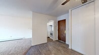 This single-floor unit offers a practical and well-organized layout across its main living spaces. The entryway, finished with durable wood-look flooring, opens into a central area connecting the kitchen and living room. The kitchen is efficiently designed with white cabinetry, ample upper and lower storage, a double-basin sink, a white appliance suite including an electric range and refrigerator, and a pass-through counter that overlooks the carpeted living area — creating an open, connected feel.

The living room is generously sized, featuring soft wall-to-wall carpeting, a ceiling fan, a textured ceiling, and a large sliding glass door that leads to a private balcony. The balcony provides views of the surrounding neighborhood and fills the space with natural light.

The bedroom is a comfortable, carpeted room with a ceiling fan, a window allowing additional natural light, baseboard heating, and a wide sliding-door closet offering ample storage. The full bathroom is finished with classic white tile in the tub surround and on the floor, a standard tub-shower combo, a toilet, and a wood-toned vanity. Throughout the unit, baseboard heating is present, ensuring year-round comfort.