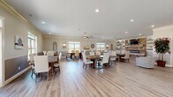 Located at 820 South Gateway Plaza Boulevard in Clarksville, Tennessee, this single-story community clubhouse offers a generous, open-concept layout designed for gathering and socializing. The main area is anchored by multiple large farmhouse-style dining tables with upholstered, nail-head-trim chairs, providing ample communal seating throughout the space. Light hardwood-style flooring runs continuously underfoot, complementing the warm, neutral color palette of the walls and décor.

A standout feature is the full-service kitchen, appointed with gray shaker-style cabinetry, white quartz countertops, subway tile backsplash, stainless steel appliances, a large center island, and open floating shelves. A picture window over the sink fills the kitchen with natural light and views of the surrounding community.

The lounge area offers a comfortable sectional sofa, accent chairs, and a striking floor-to-ceiling brick fireplace with a wall-mounted television and rustic floating shelves. Crown molding and two-tone wainscoting walls add architectural refinement throughout.

Large windows on multiple sides of the building invite abundant natural light and outdoor views, while ceiling fans provide additional comfort. Recessed lighting and pendant fixtures ensure the space is well-illuminated at all hours, creating a welcoming and functional environment for residents.