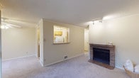 This single-floor residence offers a practical and comfortable layout with distinct living, sleeping, kitchen, and bathroom areas. The living room serves as the centerpiece of the home, featuring plush wall-to-wall carpeting, crown molding, and a classic brick fireplace that adds warmth and character. Track lighting illuminates the space, while a large sliding glass door with vertical blinds allows abundant natural light and provides access to an outdoor area with a view of surrounding greenery. A pass-through window connects the living room to the kitchen, enhancing the open feel of the shared space. The galley-style kitchen is efficiently designed with warm wood cabinetry, laminate countertops, a stainless steel sink, and white appliances including a range, oven, and refrigerator. Tile flooring runs throughout the kitchen, providing easy maintenance. The bedroom is generously sized with soft carpeting, a window with vertical blinds for natural light and privacy, and a double sliding-door closet offering ample storage. The bathroom features tile flooring, a combination tub and shower with a curtain, and a wood-trimmed vanity. Throughout the residence, neutral tones create a cohesive and inviting atmosphere.