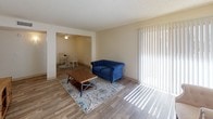 This single-floor unit offers a practical and cohesive layout designed for comfortable everyday living. Wood-look vinyl flooring runs throughout the space, providing a consistent, low-maintenance foundation that ties each area together seamlessly.

The living room is bright and open, featuring a sliding glass door with vertical blinds that allows ample natural light to fill the room. It connects directly to the dining area, which is accented by a ceiling fan overhead, creating a fluid, open-plan feel ideal for both relaxing and entertaining.

The galley-style kitchen is efficiently organized, featuring rich dark wood cabinetry on both sides, light speckled countertops, a double-basin sink, and white appliances including a range and refrigerator. The layout maximizes counter and storage space within a compact footprint.

The bedroom is a calm, neutral space with cream-toned walls, a textured ceiling, and a window that brings in natural light and outdoor views of surrounding greenery.

The bathroom includes a full tub and shower combination with a decorative curtain, a dark wood vanity with a speckled countertop, and wood-look flooring that complements the rest of the unit. Overall, the space presents a clean, functional aesthetic throughout.