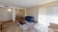 This single-floor unit offers a practical and cohesive layout designed for comfortable everyday living. Wood-look vinyl flooring runs throughout the space, providing a consistent, low-maintenance foundation that ties each area together seamlessly.

The living room is bright and open, featuring a sliding glass door with vertical blinds that allows ample natural light to fill the room. It connects directly to the dining area, which is accented by a ceiling fan overhead, creating a fluid, open-plan feel ideal for both relaxing and entertaining.

The galley-style kitchen is efficiently organized, featuring rich dark wood cabinetry on both sides, light speckled countertops, a double-basin sink, and white appliances including a range and refrigerator. The layout maximizes counter and storage space within a compact footprint.

The bedroom is a calm, neutral space with cream-toned walls, a textured ceiling, and a window that brings in natural light and outdoor views of surrounding greenery.

The bathroom includes a full tub and shower combination with a decorative curtain, a dark wood vanity with a speckled countertop, and wood-look flooring that complements the rest of the unit. Overall, the space presents a clean, functional aesthetic throughout.