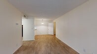 This well-organized one-bedroom, one-bathroom unit is laid out across a single floor, offering a practical and comfortable living arrangement. The entry opens into a bright living area with light wood-look laminate flooring, neutral white walls, and a textured ceiling. A pendant light fixture over the pass-through counter marks the transition into the kitchen, which features a classic galley layout equipped with warm honey-toned cabinetry, granite-style countertops, a double-basin sink, and black appliances including an electric range and full-size refrigerator. The open dining and living area provides a clean, versatile space with room for multiple furniture configurations. A hallway connects the main living area to the private bedroom, which features medium-toned wood-look flooring, a wide window with views of surrounding greenery, and a louvered bifold closet with built-in shelving for organized storage. The bathroom is thoughtfully appointed with a wood-vanity cabinet, granite-style countertop, a full tub-shower combination, and coordinating wood-look flooring. Throughout the unit, consistent flooring and a neutral color palette create a cohesive, clean aesthetic that is both functional and easy to personalize.