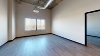 Located at 215-219 S Water St in Henderson, NV, this 1-bedroom, 2-bathroom unit offers a striking blend of modern design and industrial character. Soaring ceilings with exposed ductwork lend an urban loft aesthetic throughout, while large windows invite abundant natural light and outdoor views into the living spaces.

The kitchen is a standout feature, showcasing rich dark wood cabinetry, open floating shelves, light quartz countertops, and a central island with a built-in sink. Stainless steel appliances — including a range with a wall-mounted hood, refrigerator, and dishwasher — complete the space, all set atop light hardwood flooring with sleek pendant lighting overhead.

The generously sized primary bedroom features plush carpeting, impressively tall ceilings with exposed ductwork, mirrored sliding closet doors, and a window that fills the room with natural light. An additional flexible room, also carpeted with high ceilings and a window, provides versatile space suitable for a home office or den.

Both bathrooms are finished with light tile flooring and dark wood vanities topped with white quartz counters. The primary bath includes a tub-shower combination with white tile surround and an LED-lit medicine cabinet mirror, while the second bath offers a clean, functional layout. A hallway connects the rooms efficiently, completing this well-designed urban residence.