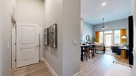 This thoughtfully designed one-bedroom, one-bathroom residence offers an efficient yet comfortable single-floor layout. The open-concept living and dining area immediately impresses with soaring ceilings and an abundance of natural light streaming through large windows dressed with floor-length curtains and a glass-panel entry door, creating a bright and airy ambiance throughout. Light wood-style flooring flows seamlessly across the main living spaces.

The kitchen is a standout feature, boasting tall white cabinetry that maximizes vertical storage, a classic subway tile backsplash, stainless steel appliances including a range, microwave, and dishwasher, and a sleek kitchen island with a marble-style countertop and bar seating — ideal for casual dining or entertaining.

The primary bedroom offers a tranquil retreat with plush carpeting, a generous window overlooking the outdoors, and direct access to a well-sized walk-in closet outfitted with wire shelving and hanging rods for organized storage. The full bathroom features a tub-shower combination with tile surround and modern fixtures.

A dedicated laundry room with a full-size washer and dryer adds everyday convenience. A welcoming hallway connects each room, with art-ready wall space and neutral tones that lend the entire residence a clean, contemporary feel.