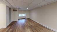 Located at 40 Beach St in Boston's Chinatown neighborhood, this single-floor unit offers a straightforward, functional layout with consistent finishes throughout. The main living areas feature warm wood-look plank flooring and cream-toned walls beneath a drop tile ceiling with recessed and panel lighting. Small windows allow modest natural light into the space, supplemented by overhead fixtures.

The kitchen is appointed with rich dark-espresso cabinetry extending to the ceiling, providing generous storage. Light granite countertops and a stainless steel sink offer a clean contrast, while a gas range with an overhead ventilation hood completes the cooking area. Light ceramic tile flooring grounds the kitchen space distinctly from the rest of the unit.

A closet with a rod provides dedicated storage, and a black refrigerator is also included. The bathroom continues the granite countertop theme at the vanity, paired with a wall-mounted mirror. White subway tile lines the walls, complementing a combined tub and shower setup with chrome fixtures, creating a clean and cohesive aesthetic. The overall layout is open and adaptable, suited for a variety of uses in a central Boston location.