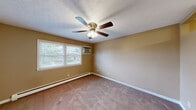 Located at 708 Fairmont #7 on Arcadia Drive in Bloomington, Illinois, this 2-bedroom, 1-bathroom unit offers a practical and comfortable single-floor layout. The living room serves as the heart of the home, featuring warm neutral-toned walls, plush carpeting, a ceiling fan with integrated lighting, and an open sightline into the kitchen. The kitchen is outfitted with dark wood cabinetry, a white refrigerator, and a gas range, with tile-style flooring that contrasts the carpeted living areas. The generously sized primary bedroom is one of the standout features of this unit, offering ample floor space, a ceiling fan with light fixture, a built-in closet with sliding doors, and a baseboard heating unit. The second bedroom is similarly appointed with carpeting, a ceiling fan, a window allowing natural light and outdoor views, and baseboard heating. The full bathroom includes a tub and shower combination with tiled surround walls and chrome fixtures, maintaining a clean and functional aesthetic throughout. Neutral beige tones unify the space, giving it a cohesive and understated character. The overall layout is efficient and well-suited for comfortable everyday living.