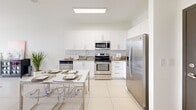This 610 square foot apartment in West Miami offers a thoughtful blend of functionality and style. The single-floor layout comprises two bedrooms, one bathroom, a kitchen, and a closet, efficiently utilizing every inch of space. The primary bedroom, spanning 170 square feet, provides ample room for comfort and relaxation.

The bathroom features clean lines with large, neutral-toned tiles, a bathtub-shower combination, and modern fixtures. The kitchen impresses with its contemporary design, boasting sleek white cabinetry, stainless steel appliances, and granite countertops. It includes a built-in microwave, range, and refrigerator, complemented by a dining area with a modern table and transparent chairs.

Both bedrooms are well-appointed, with the larger room showcasing a tufted headboard, matching side tables, and stylish lighting fixtures. Large windows in the bedrooms allow natural light to flood the space, creating an airy atmosphere. The rooms feature light wood flooring, adding warmth to the overall design.

The apartment's cohesive color scheme of whites, grays, and light wood tones creates a sense of spaciousness and modernity throughout. Ceiling fans and recessed lighting further enhance the comfort and ambiance of this compact yet well-designed living space.