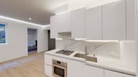 Located at 7901–7925 W First St in the heart of Los Angeles, this single-floor space showcases a thoughtfully designed modern interior with a clean, minimalist aesthetic throughout. The kitchen is a standout feature, outfitted with flat-front white cabinetry, brushed gold hardware, and a striking veined marble slab backsplash that extends the full length of the counter. Stainless steel appliances — including a gas cooktop, built-in oven, and undermount sink with a gooseneck faucet — complete the highly functional culinary space. Recessed LED strip lighting beneath the upper cabinets adds a refined, contemporary glow. The open living area continues the minimalist theme with smooth white walls, light wood-tone flooring, and elegant LED cove lighting that traces the ceiling perimeter, creating a warm and inviting ambiance. A window allows natural light to filter in, providing a view of the surrounding exterior. Built-in wall-mounted shelving and media provisions offer practical yet stylish solutions for everyday living. The bathroom features a frameless glass-enclosed walk-in shower with large-format concrete-look tile surround, mosaic tile flooring, and polished chrome fixtures, delivering a spa-inspired experience. A warm wood entry door with a modern black frame adds a welcoming contrast upon entry.