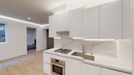 Located at 7901–7925 W First St in the heart of Los Angeles, this single-floor space showcases a thoughtfully designed modern interior with a clean, minimalist aesthetic throughout. The kitchen is a standout feature, outfitted with flat-front white cabinetry, brushed gold hardware, and a striking veined marble slab backsplash that extends the full length of the counter. Stainless steel appliances — including a gas cooktop, built-in oven, and undermount sink with a gooseneck faucet — complete the highly functional culinary space. Recessed LED strip lighting beneath the upper cabinets adds a refined, contemporary glow. The open living area continues the minimalist theme with smooth white walls, light wood-tone flooring, and elegant LED cove lighting that traces the ceiling perimeter, creating a warm and inviting ambiance. A window allows natural light to filter in, providing a view of the surrounding exterior. Built-in wall-mounted shelving and media provisions offer practical yet stylish solutions for everyday living. The bathroom features a frameless glass-enclosed walk-in shower with large-format concrete-look tile surround, mosaic tile flooring, and polished chrome fixtures, delivering a spa-inspired experience. A warm wood entry door with a modern black frame adds a welcoming contrast upon entry.