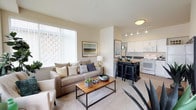 This single-floor residence offers a thoughtfully designed layout with a comfortable, open-concept living and kitchen area. The living room is bright and welcoming, featuring large windows with vertical blinds that allow generous natural light to fill the space, along with a glass patio door providing direct outdoor access and views of the surrounding neighborhood. Plush carpeting and neutral wall tones create a warm, inviting ambiance throughout.

The kitchen is efficiently arranged in a galley-style configuration, featuring white cabinetry, dark countertops, and a full suite of white appliances including a refrigerator, range, microwave, and dishwasher. Track lighting overhead adds both style and functionality. A breakfast bar provides additional seating and connects seamlessly to the living area.

The residence includes two bedrooms, each carpeted and equipped with ceiling fans. The primary bedroom is generously sized and connects to a private en-suite bathroom featuring a wide vanity with dark countertops, a large mirror, and hardwood-style flooring. A second full bathroom with similar finishes serves the additional bedroom. Both bedrooms offer comfortable proportions and ample room for furnishings, making this a practical and well-balanced living space.