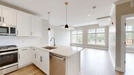 Located at 445 South Ave E in Westfield, NJ, this well-appointed 2-bedroom, 2-bathroom residence offers a thoughtfully designed single-floor layout with generous living space throughout. The open-concept kitchen, dining, and living area serves as the heart of the home, featuring light hardwood-style flooring, large windows that invite abundant natural light, and views of the surrounding area. The kitchen is outfitted with crisp white shaker cabinets, quartz countertops, a central island with an undermount sink, stainless steel appliances including a gas range, dishwasher, microwave, and refrigerator, and stylish gold pendant lighting. The living area flows seamlessly from the kitchen and connects to a private balcony. Both bedrooms are well-sized, with the primary bedroom offering notable square footage, light-toned walls, and access to ample closet storage via built-in shelving and hanging rods across three closets. The two bathrooms are distinctly finished — one features marble-look tile, a soaking tub, and a white vanity, while the other includes a double-sink vanity with dark countertops and tile flooring. Neutral warm-gray paint tones, recessed lighting, and white panel doors complete the clean, modern aesthetic throughout.