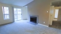 This single-floor space offers a thoughtfully designed living area that combines comfort and functionality. The living room serves as the focal point of the home, highlighted by a classic tile-surround fireplace set against a warm-toned accent wall, creating an inviting atmosphere ideal for relaxing or entertaining. Vaulted ceilings rise overhead, lending the space a generous sense of height and openness that enhances the overall feel of the room. Soft, plush wall-to-wall carpeting covers the floor throughout, adding warmth and comfort underfoot. A large sliding glass door floods the interior with natural light and provides direct access to a private outdoor balcony, where views of surrounding trees can be enjoyed. The balcony is equipped with a classic railing, offering a pleasant outdoor retreat. Neutral wall tones and clean white trim complement the interior's understated, practical aesthetic. The layout is open and unobstructed, allowing for flexible furniture arrangements to suit a variety of needs. Overall, this space presents a comfortable and well-lit environment with key features that balance everyday livability with welcoming design details.
