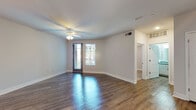 This single-floor unit offers a well-designed layout with modern finishes throughout. The living area is bright and open, featuring rich, dark hardwood-style flooring, clean white walls, and a ceiling fan with light fixture. A glass-paneled door floods the space with natural light and provides outdoor access, while the polished floors reflect the ambient light for a welcoming atmosphere.

The kitchen is a standout feature, designed with functionality and style in mind. It includes a central island with a granite-style countertop, an undermount sink, and pendant lighting overhead. White cabinetry lines the walls, complemented by a light blue subway tile backsplash. Stainless steel appliances — including a gas range with double oven, built-in microwave, dishwasher, and a French door refrigerator with ice and water dispenser — complete the contemporary look.

A dedicated laundry area houses a stacked washer and dryer unit, conveniently tucked alongside additional storage. The entryway features a stylish two-panel gray door with track lighting overhead, adding to the modern aesthetic.

The bathroom is clean and well-appointed, with granite-topped vanity cabinetry, a large mirror, and a glass-enclosed walk-in shower with tiled walls. Hardwood-style flooring continues throughout, maintaining a cohesive design across the entire space.