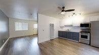 Located at 630 Magnolia Ave in Long Beach, California, this efficiently designed single-floor unit offers a thoughtfully laid-out open-plan living space. Wood-look plank flooring runs throughout, providing a cohesive, contemporary feel that ties all areas together seamlessly.

The combined living and kitchen area forms the heart of the unit. The kitchen is well-appointed with a two-tone cabinet design — white upper shaker-style cabinets paired with slate-gray lower cabinets — complemented by a clean white countertop and white subway tile backsplash. A full suite of stainless steel appliances includes a gas range, over-the-range microwave, and a full-size refrigerator. A ceiling fan with integrated lighting and a track lighting fixture illuminate the open living area, which benefits from natural light through a large window fitted with vertical blinds.

A second room, currently open and flexible in use, features a textured dark accent wall and an additional window, offering versatility for various living arrangements. The bathroom is clean and minimal, with light wood-look flooring, white walls, and a vanity with dark cabinetry consistent with the kitchen's design language. The unit also includes a wall-mounted HVAC unit for climate control. Overall, the space presents a modern, freshly updated interior suitable for efficient urban living in the heart of Long Beach.