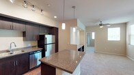 This single-floor residence offers a thoughtfully designed layout with modern finishes throughout. The kitchen serves as the heart of the home, showcasing rich dark cabinetry, granite countertops, and a full suite of stainless steel appliances including a refrigerator, range, microwave, and dishwasher. A large kitchen island provides additional prep space and casual seating, while pendant lighting and track lighting illuminate the area. Hardwood-style flooring runs through the kitchen, complementing the warm, contemporary aesthetic.

The living area flows naturally from the kitchen and features plush carpeting and a ceiling fan, creating a comfortable, functional space. The bedrooms are carpeted and well-sized, each equipped with ceiling fans and closet storage. One bedroom features mirrored sliding closet doors, while another includes a walk-in style closet with built-in shelving and rod systems, along with direct access to an outdoor balcony with green views.

Two bathrooms serve the residence — one featuring a walk-in shower with sliding glass doors and hardwood-style flooring, and the other offering a full tub-shower combination with chrome fixtures. A dedicated in-unit laundry room accommodates a full-size washer and dryer with additional shelving for storage, adding everyday convenience to this well-rounded home.