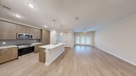 Located at 4434 Cobalt Brook Boulevard in Lutz, FL, this well-appointed single-floor residence offers a thoughtfully designed open-concept layout that seamlessly connects the kitchen, dining, and living areas. Light wood-style flooring flows throughout the entire space, creating a cohesive and modern aesthetic.

The kitchen is a standout feature, boasting a central island with a white quartz countertop and built-in sink, pendant lighting, warm wood-toned cabinetry extending to the ceiling, a gray subway tile backsplash, and a full suite of stainless steel appliances including a refrigerator, range, and microwave. Ample cabinet storage ensures excellent functionality.

The living area is bright and airy, featuring a ceiling fan and French doors that invite natural light and provide outdoor access. The bedroom is a comfortable retreat with a ceiling fan, a large window with views of lush greenery, and two closets — including a walk-in closet fitted with multi-tier wire shelving for generous storage.

The bathroom offers a clean, modern design with wood-toned cabinetry, white countertops, a combined tub and shower, and wood-style flooring. A dedicated laundry area completes this efficiently organized residence.