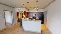 Located at 701 Leora Ln in Lewisville, Texas, this single-story residence presents a thoughtfully designed interior with a consistent aesthetic carried throughout its living spaces. The kitchen serves as a focal point of the home, showcasing rich warm-toned wood cabinetry that extends to the ceiling, providing generous storage capacity. Granite countertops with subtle veining run along the perimeter and continue onto a peninsula-style island, which offers additional prep space and a natural transition into the main living area. Black appliances, including a refrigerator, electric range, built-in microwave, and dishwasher, complement the cabinetry. A tile backsplash adds texture, while a combination of track lighting and suspended pendant fixtures ensures ample illumination throughout the kitchen.

The living area is open and airy, featuring light hardwood-style flooring that extends throughout the unit. Multiple windows allow natural light to flow in, offering exterior views, and a ceiling fan provides added comfort. The bedroom continues the same flooring and neutral color palette, with a window and ceiling fan lending a bright, functional feel. The bathroom is equipped with a tub-shower combination, a vanity with warm wood cabinetry, light countertops, a large mirror, and overhead wall-mounted storage. The overall ambiance is clean, modern, and cohesive.