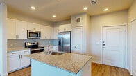 This well-appointed single-floor residence showcases a thoughtfully designed open-concept layout, seamlessly connecting the kitchen and living areas for an inviting, functional flow. The kitchen serves as the heart of the home, featuring crisp white shaker cabinetry extending to the ceiling for generous storage, light blue subway tile backsplash, and granite countertops that carry across both the perimeter surfaces and the spacious central island. The island includes a undermount sink and provides ample prep space and casual seating potential. A full suite of stainless steel appliances — including a side-by-side refrigerator with ice and water dispenser, electric range, and over-the-range microwave — complete the kitchen's modern aesthetic. Light wood-tone luxury vinyl plank flooring runs throughout the main living areas and bedrooms, lending warmth and continuity to the space. The bedrooms are bright and airy, each featuring ceiling fans and windows fitted with white blinds that allow for natural light. The bathrooms are finished with matching granite vanity tops, white cabinetry with brushed nickel hardware, and large mirrors framed by vanity lighting. The full bath includes a soaking tub with a marble-style tiled surround. Recessed lighting and neutral wall tones throughout create a clean, contemporary ambiance.