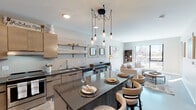 This single-floor residence showcases a thoughtfully designed open-concept layout that seamlessly connects the kitchen, dining, and living areas into one cohesive and inviting space. The kitchen is a standout feature, equipped with flat-front light wood cabinetry, dark stone countertops, stainless steel appliances, and a vertically tiled backsplash. A central island with seating serves as both a functional prep area and a casual dining spot, illuminated overhead by a striking multi-bulb pendant chandelier with an industrial aesthetic. Polished concrete flooring runs throughout the main living area, adding a contemporary edge. The living room offers a comfortable, neutral-toned sectional sofa, warm wood accents, and a large window that invites abundant natural light and urban views. The bedroom is a calm retreat featuring plush carpeting, large sliding glass doors that open to an outdoor balcony with city views, and modern flat-panel interior doors. The bathroom is finished with dark stone countertops, a wood-toned vanity, a large mirror with modern sconce lighting, and a separate shower area. Throughout the space, the design palette of warm neutrals, natural wood tones, and dark metal accents creates a cohesive and contemporary atmosphere.