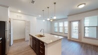 This single-story residence on Whaley Drive in Forney, Texas presents a thoughtfully designed open-concept layout that seamlessly integrates the kitchen, dining, and living areas. The kitchen serves as the centerpiece of the home, anchored by a generously sized island topped with granite countertops, an undermount sink, and pendant lighting overhead. Dark espresso cabinetry provides strong visual contrast against the light countertops, while stainless steel appliances — including a refrigerator, range, and microwave — complete the well-appointed cooking space. A white subway tile backsplash adds a clean, classic touch behind the range.

Wood-look flooring extends throughout the main living areas, lending warmth and cohesion to the space. The open living area benefits from multiple windows that invite natural light and offer views of the surrounding neighborhood. Ceiling fans are present in both the living area and bedroom, contributing to everyday comfort.

The bedroom features plush carpeting and dual windows that brighten the room naturally. The bathroom is finished with matching granite countertops on dark cabinetry and includes a glass-enclosed walk-in shower with tile surround. A walk-in closet with built-in shelving provides practical storage. Crown molding and recessed lighting add refined finishing touches throughout.