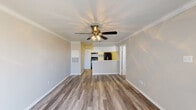 This single-story unit in Spring, Texas, presents a thoughtfully laid-out interior with a clean, updated aesthetic throughout. The main living area is an open, welcoming space finished with wood-look luxury vinyl plank flooring that extends seamlessly toward the kitchen. Crown molding frames the ceiling, and a ceiling fan with a light fixture provides both function and a finishing detail. A half-wall peninsula connects the living space to the kitchen, creating an open-concept feel while maintaining a defined cooking zone.

The kitchen is outfitted with white cabinetry featuring updated hardware, a white subway tile backsplash, white laminate countertops, and black appliances including an electric range, range hood, and refrigerator. The wood-look flooring continues into this space, maintaining visual continuity.

The bedroom is carpeted and comfortably scaled, with a window dressed in blinds that allows natural light to filter in. A ceiling fan overhead adds to the room's comfort.

The bathroom is finished with wood-look flooring, a white vanity with updated hardware, a toilet, and a tub-shower combination with white tile surround. The overall unit carries a neutral, updated palette that lends it a fresh and functional character.