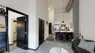 This contemporary single-floor loft showcases an industrial-modern aesthetic that is both striking and functional. Soaring ceilings draw the eye upward, creating an expansive, airy atmosphere throughout the open-concept living space. Polished concrete floors run seamlessly underfoot, adding an industrial edge that complements the overall design language.

The kitchen is a standout feature, boasting crisp white cabinetry paired with a dramatic dark island topped with a light countertop. A row of black-and-gold bar stools lines the island, making it an ideal spot for casual dining or entertaining. Stainless steel appliances, including a refrigerator and microwave, are neatly integrated into the cabinetry, while pendant lighting hangs above the island to provide focused illumination and a touch of modern elegance.

Bold black interior doors with clean panel detailing create strong visual contrast against the bright white walls, reinforcing the space's monochromatic design theme. Exposed ceiling infrastructure adds an authentic loft character, enhancing the sense of height and openness. The living area provides a welcoming transition from the kitchen, anchored by a patterned area rug and a marble-top accent table. Overall, this space delivers a refined yet edgy urban living experience.