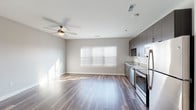 Located at 1010 Enclave Blvd in Edwardsville, Illinois, this modern single-floor unit offers a clean, contemporary design with a cohesive aesthetic carried throughout every room. Rich wood-style plank flooring runs continuously across the entire space, providing warmth and visual continuity against the neutral gray walls and crisp white trim.

The open living area is bathed in natural light from a large multi-pane window dressed with white horizontal blinds, while a ceiling fan overhead ensures year-round comfort. The space flows seamlessly into the kitchen, which is outfitted with dark espresso-toned cabinetry extending to the ceiling, light granite countertops, a white subway tile backsplash, and a full suite of stainless steel appliances including a refrigerator, range, microwave, and dishwasher.

The bedroom is generously proportioned, featuring its own ceiling fan, a wide closet with double doors, and additional natural light from a bright window. Convenient access to a hallway with additional storage adds to the unit's functional layout.

The bathroom continues the modern design language with dark cabinetry, a white vanity top, and wood-style flooring. The overall ambiance of the space is bright, clean, and move-in ready, reflecting a thoughtfully designed and well-appointed interior.