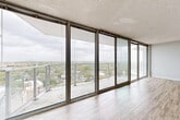 Located in Norfolk, Virginia, this one-bedroom, one-bathroom high-rise residence offers a well-designed layout across a single floor. The living room is an immediate standout, featuring a dramatic wall of floor-to-ceiling sliding glass doors that open to a balcony, flooding the space with natural light and framing sweeping panoramic views of the Norfolk cityscape and surrounding landscape. Light-toned hardwood-style flooring runs throughout the living area, complementing the neutral walls and textured ceiling.

The kitchen is well-appointed with white shaker cabinetry, granite-style countertops, a classic subway tile backsplash, and stainless steel appliances including a gas range and built-in microwave. The galley-style layout maximizes efficiency while maintaining a clean, modern aesthetic.

The spacious primary bedroom is carpeted for comfort and features a wide picture window with horizontal blinds offering additional city views, along with a set of bi-fold closet doors providing ample storage. A separate walk-in closet area is also accessible from the bedroom.

The bathroom includes a tub-shower combination enclosed by a sliding glass door, a toilet, and hardwood-style flooring, maintaining a clean and functional design throughout.