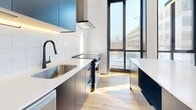 Located at 3555 Saint-Antoine O in Montreal, this modern 3-bedroom, 1-bathroom unit showcases contemporary design with clean lines and a bright, open atmosphere. Warm hardwood-style flooring runs throughout, complementing the crisp white walls and creating a cohesive, inviting aesthetic.

The open-concept dining and living area is a standout feature, bathed in abundant natural light through dramatic floor-to-ceiling black-framed windows that offer views of the surrounding neighbourhood. The kitchen is sleekly designed with navy blue cabinetry, white countertops, a white tile backsplash, stainless steel appliances, a built-in range hood, and a matte black faucet — with a large island providing additional workspace and a bold design statement.

The three bedrooms are bright and airy, each benefiting from large windows that invite natural light, with the primary bedroom offering generous proportions. A slim hallway with recessed track lighting connects the rooms efficiently.

The bathroom is finished to a modern standard, featuring large-format beige floor tiles, a sliding glass-enclosed shower with white subway tiles and black fixtures, a wood-toned vanity, and a round mirror. Two closets and an in-unit laundry area complete the practical amenities of this well-appointed urban residence.