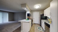 This single-floor residence at Northland Passage in Kansas City, Missouri offers a practical and well-appointed layout designed for comfortable everyday living. The kitchen serves as a central feature of the unit, showcasing white cabinetry, granite-style countertops, and a peninsula island that provides additional prep space and seating potential. Stainless steel appliances, including a refrigerator, range, microwave, and dishwasher, are integrated throughout. Light wood-style flooring runs through the kitchen and connects seamlessly to adjacent areas, while recessed lighting and a flush-mount ceiling fixture provide ample illumination.

The living area transitions naturally from the kitchen, featuring neutral-toned carpet, warm gray walls, and a large sliding glass door fitted with vertical blinds that allow natural light to filter in and offer access to an outdoor space. The bedrooms continue the carpeted aesthetic, each with neutral walls, textured ceilings, and windows dressed with horizontal blinds that invite natural light.

The bathroom includes a granite-topped vanity with white cabinetry, wood-style flooring, an overhead storage cabinet, and a full tub-and-shower combination with tile surround. A soaking tub is also present, adding a noteworthy amenity. Overall, the unit presents a cohesive, neutral palette with modern finishes throughout.