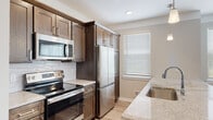 This two-floor residence presents a well-designed layout with modern finishes throughout. The heart of the main level is an open-concept kitchen and living area, where light hardwood-style flooring extends seamlessly across the space. The kitchen is outfitted with rich, dark wood cabinetry reaching toward the ceiling, a classic white subway tile backsplash, and a full suite of stainless steel appliances, including a refrigerator, range, and built-in microwave. Light granite countertops provide ample prep space, and a peninsula with an integrated sink doubles as a breakfast bar, illuminated by pendant lighting above. Multiple windows fitted with horizontal blinds allow natural light to fill both the kitchen and the adjoining living area.

The bathroom features floor-to-ceiling tile surrounding a soaking tub and shower combination, complemented by granite countertops on the wood-toned vanity and neutral tile flooring throughout. Bedrooms are carpeted in a neutral tone and receive natural light through well-placed windows. A dedicated laundry area houses a full-sized washer and dryer with overhead shelving for additional storage, adding practical convenience to the overall layout.