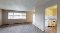 Located at 13795 SW Electric St in Beaverton, Oregon, this single-floor unit offers a practical and well-organized layout suited for comfortable everyday living. The living area is generously sized, featuring wall-to-wall carpet, a textured ceiling, and large windows fitted with blinds and vertical panel coverings that allow natural light to fill the space. Baseboard heaters line the walls, providing efficient heating throughout. The kitchen is equipped with a peninsula countertop offering additional prep space, white cabinetry, dark laminate countertops, a range, dishwasher, and a full-size refrigerator. Tile flooring runs through the kitchen and connects to the adjacent hallway and bathroom. The two bedrooms are carpeted and each features a window for natural light and closet access, with one bedroom offering a standard reach-in closet with a hanging rod. A dedicated hallway closet provides additional built-in shelving and storage. The full bathroom includes a wide vanity with a dark countertop, white cabinetry, a large mirror with overhead lighting, tile flooring, and a shower-tub combination. The overall design is clean and functional, offering a neutral palette throughout.