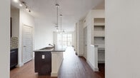 This single-story, one-bedroom, one-bathroom residence offers a thoughtfully designed layout that maximizes functionality and style. The open-concept kitchen and living area serves as the heart of the home, featuring rich wood-look flooring, crisp white walls, and an abundance of natural light from large windows and a sliding glass door. The kitchen is equipped with dark espresso cabinetry, granite countertops, stainless steel appliances including a refrigerator, range, and built-in microwave, and a mosaic tile backsplash. A central island with an integrated sink and pendant lighting above adds both workspace and visual appeal.

The living area flows seamlessly from the kitchen, offering a bright, open environment with a ceiling fan. A hallway connects the main living spaces to the private bedroom wing. The bedroom is generously sized, finished with plush wall-to-wall carpeting and dual windows that invite natural light. It provides direct access to a full bathroom and a spacious walk-in closet outfitted with multiple shelving units and hanging rods.

The bathroom features large-format tile flooring, a soaking tub with a tiled surround accented by a decorative border, a dark vanity with granite countertop, and a mirror with overhead lighting. This residence combines practical storage solutions with modern finishes throughout.