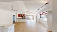 This single-floor home is defined by its striking vaulted ceilings that soar over a generously proportioned open-concept living and dining area, creating an airy, expansive atmosphere throughout. Light hardwood-style flooring flows across the main living spaces, enhancing the sense of openness. A ceiling fan and rail lighting system complement the natural light that pours in through large sliding glass doors leading to an outdoor patio area.

The kitchen is a standout feature, showcasing rich cherry wood cabinetry, dark granite countertops, stainless steel appliances including a refrigerator and gas range, and a breakfast bar that opens directly to the main living area — ideal for entertaining.

A dedicated flex room offers a distinctive design highlight: an expansive skylight window with red-framed louvers and built-in shelving, making it well-suited for use as a home office, studio, or reading nook.

Bedrooms are carpeted and filled with natural light, with one featuring a spacious walk-in closet with full rod and wire shelving. The bathroom is finished with tile flooring, a cherry wood vanity, white countertop, and a tub-shower combination. Additional utility areas include an in-unit washer, and the home also features a garage with visible HVAC and utility systems.