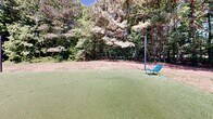 Located at 1000 Park Place Ave in Morrisville, North Carolina, this outdoor amenity space offers a well-appointed and inviting environment designed for relaxation and recreation. The space is framed by mature trees and dense natural greenery, creating a serene, park-like atmosphere that feels both private and open.

A standout feature is the synthetic putting green, providing a smooth, well-maintained surface ideal for casual golf practice. Nearby, a pergola structure serves as a covered gathering area, outfitted with comfortable outdoor seating and anchored by string lights that lend a warm, social ambiance during evening hours. Adjacent to the pergola, a concrete patio extends the usable outdoor space, accommodating additional seating arrangements for lounging or socializing.

The expansive open lawn area offers generous green space for a variety of outdoor activities, bordered by natural wooded edges that provide shade and a sense of seclusion. String lights are strung across poles throughout the space, adding a charming aesthetic touch that transitions seamlessly from day to night use. A utility structure with warm wood cladding is also present on-site, complementing the natural surroundings. The overall design balances functional recreational amenities with a relaxed, nature-integrated setting, making it an appealing outdoor destination.