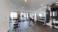 This fitness center offers a comprehensive workout environment designed to support a range of exercise routines. The space is finished with durable rubber flooring, providing both safety and comfort during training sessions. Recessed lighting throughout the ceiling ensures the room is well-lit, while large windows along the perimeter walls allow natural light to fill the space, creating an open and energizing atmosphere.

A full wall of floor-to-ceiling mirrors lines one side of the room, visually expanding the space and allowing users to monitor their form during exercise. The cardio section is well-appointed with multiple treadmills and elliptical machines, each equipped with individual display screens for tracking workout metrics. A dedicated free weights area features a complete dumbbell rack with a wide range of weight options, accompanied by an adjustable workout bench for strength training. Additional strength and conditioning equipment, including a multi-function exercise station, rounds out the equipment offering. The clean, modern aesthetic and thoughtful layout make this fitness center a functional and inviting space for residents to pursue their health and wellness goals.