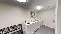 Located at 700 Saint Marys Ave in Frankfort, Indiana, this single-floor shared laundry facility offers a practical and well-maintained space designed for everyday convenience. The room features a row of top-load washing machines lined along one wall, providing ample capacity to accommodate multiple users. The interior is finished with neutral-toned walls and carpeted flooring, creating a clean and welcoming environment. Overhead flush-mount lighting ensures the space is brightly illuminated, complemented by a textured ceiling that adds a subtle design detail. A decorative framed artwork hangs on the wall, adding a touch of warmth and personality to what is typically a purely utilitarian space. An ornate black metal bench is positioned near the entrance, offering a comfortable place to sit while waiting. The layout is straightforward and functional, making it easy to navigate. Overall, the laundry facility strikes a balance between practicality and comfort, maintaining a tidy and inviting atmosphere that enhances the day-to-day experience for its users.