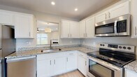 Located at 3884 N Chalet Cir in Beavercreek, Ohio, this two-story home offers a well-designed layout with modern finishes throughout. The kitchen is a standout feature, showcasing crisp white shaker-style cabinetry, granite countertops, light hardwood-style flooring, and a full suite of stainless steel appliances including a refrigerator, electric range, microwave, and dishwasher. A pass-through opening connects the kitchen to the adjacent living area, enhancing the open feel of the main level. The living room is bright and inviting, with light hardwood-style flooring, recessed lighting, a ceiling fan, a fireplace with a white mantel, and sliding glass doors that bring in abundant natural light and provide outdoor access. Bathrooms are finished with neutral tones, granite vanity tops, and light flooring, offering a clean and functional design. Bedrooms feature plush carpeting, ceiling fans, and generous closet space with wire shelving systems. Vaulted ceilings in select rooms add to the sense of openness. A dedicated laundry area houses a full-size washer and dryer. The home's warm, neutral color palette and thoughtful layout create a comfortable and cohesive living environment across both floors.