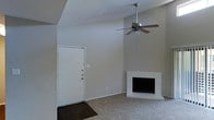 Located in Arlington, Texas, this single-story space showcases a spacious living area defined by soaring vaulted ceilings that create an open, airy atmosphere. The main living room is anchored by a white-tiled fireplace, providing a classic focal point and a cozy gathering spot. A ceiling fan suspended from the peak of the vaulted ceiling adds both functionality and visual interest to the room. The entry features dark hardwood-style flooring near the front door, which transitions into neutral carpeting throughout the living area, offering a warm and comfortable underfoot experience. The walls are finished in a soft, neutral gray tone, lending a clean and versatile backdrop throughout the space. The combination of the elevated ceiling height and understated color palette gives the living area a sense of openness and ease. Overall, the space presents a straightforward and functional layout with architectural details—such as the vaulted ceiling and fireplace—that add character and charm to this Arlington property.