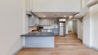 Located at 160 Seabury St in Fall River, MA, this single-floor, two-bedroom, one-bathroom unit offers a thoughtfully designed layout that makes efficient use of its space. The kitchen serves as a standout feature, showcasing gray shaker-style cabinetry, dark granite countertops, a classic white subway tile backsplash, and a full suite of stainless steel appliances including a range, microwave, dishwasher, and refrigerator. A peninsula counter provides additional workspace and helps define the kitchen area. Light-toned hardwood-style flooring runs consistently throughout the unit, lending warmth and visual continuity to every room. Both bedrooms are finished with neutral walls, clean baseboards in a soft gray tone, and double-door closets for practical storage. The primary bedroom offers a comfortable footprint with room for standard furnishings. The bathroom is spaciously configured with accessibility in mind, featuring stainless steel grab bars, light tile flooring, a curtained shower, and a vanity with granite-style countertop. A hallway connects the rooms, contributing to a clean, functional flow throughout the unit. Recessed lighting in the kitchen and neutral-toned walls throughout create a bright, modern ambiance.