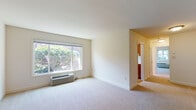 This single-floor residence offers a clean, functional layout designed for comfortable everyday living. The expansive living area is finished with neutral-toned wall-to-wall carpeting and features a large picture window that fills the room with natural light and provides views of lush greenery outside. A wall-mounted HVAC unit ensures year-round climate control, while crisp white walls and smooth ceilings give the space a bright, open feel. The entry foyer transitions seamlessly into the living area via hardwood flooring near the front door.

The kitchen is efficiently organized with warm wood cabinetry on both upper and lower sections, light-toned countertops, and hardwood flooring. White appliances — including a refrigerator, electric coil stove, built-in microwave, and dishwasher — are neatly integrated into the layout. A window above the counter brings in natural light and offers an exterior view.

The bedroom is generously sized, carpeted for comfort, and equipped with a ceiling fan with light fixture. A window frames outdoor greenery, creating a serene atmosphere. The full bathroom includes a soaking tub and shower combination with a clean white surround, a wood-toned vanity, and a frosted privacy window for natural light. Overall, the space presents a practical and well-lit living environment.