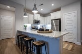 Located at City Station in Collegedale, Tennessee, this well-appointed single-story residence offers a thoughtfully designed open-concept layout with warm hardwood-style flooring throughout. The kitchen serves as the heart of the home, showcasing white shaker cabinetry, granite countertops, a central island with bar seating, stainless steel appliances, and stylish pendant lighting — all flowing seamlessly into the dining and living areas. The living room benefits from abundant natural light through large windows and French doors, creating a bright and welcoming atmosphere. Two comfortable bedrooms each feature ceiling fans, generous windows with outdoor views, and tasteful accent walls. The primary bedroom includes a dedicated en-suite bathroom with a dual-sink vanity topped in granite, white cabinetry, and a glass-enclosed walk-in shower. A second full bathroom mirrors the same refined finishes. A dedicated in-unit laundry closet with full-size washer and dryer adds everyday convenience. Throughout the residence, crisp white millwork, panel-style interior doors, and a neutral color palette create a cohesive, contemporary aesthetic that is both functional and inviting.