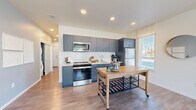 Located in University Place, WA, this well-appointed 2-bedroom, 2-bathroom residence offers a modern, single-floor layout designed for comfortable everyday living. A welcoming hallway with clean white walls and wood-look flooring draws you into the heart of the home.

The open-concept living area is bright and airy, featuring large windows that flood the space with natural light and offer outdoor views. The living room showcases a soft blue accent wall, wood-look flooring, and a wall-mounted mini-split system for year-round comfort.

The kitchen is a standout, outfitted with sleek slate-blue cabinetry, a classic white subway tile backsplash, stainless steel appliances, and generous counter space. An in-unit stacked washer and dryer add convenience.

The primary bedroom is a comfortable retreat with plush carpeting, wide windows, and ample natural light. The second bedroom mirrors this warmth, featuring a bold blue arched accent wall and large windows with outdoor views. Both bathrooms are finished with vibrant blue vanities, illuminated mirrors, white countertops, and wood-look tile flooring. A dedicated closet provides additional storage. Recessed lighting and a cohesive modern palette tie the entire space together seamlessly.