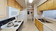 This single-floor residence offers a thoughtfully organized layout that accommodates comfortable everyday living across several distinct spaces. The living area is a standout feature, characterized by vaulted ceilings that lend an open, airy quality to the room. Neutral-toned carpet and crisp white walls create a clean backdrop, while natural light filters in through sliding glass doors fitted with vertical blinds. The space is versatile, with room for both a seating area and an entertainment setup.

The kitchen is designed for functionality, featuring a galley-style configuration with light wood cabinetry lining both walls, providing ample storage. White appliances — including a refrigerator, electric range, and microwave — complement the tile flooring. An in-unit washer is also accessible from within the kitchen corridor.

The residence includes two bedrooms, each carpeted and well-lit by windows with blinds and curtain panels. One bedroom offers a more spacious feel with room for additional seating. Both rooms maintain a calm, neutral aesthetic.

Two full bathrooms serve the unit, each featuring a single-sink vanity with a light wood cabinet base, a large mirror, and a shower-tub combination. The overall ambiance throughout is clean, functional, and cohesive.
