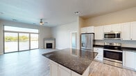 Located at 112 Papermill Run in Kimberly, Wisconsin, this well-appointed 2-bedroom, 2-bathroom single-floor residence offers a thoughtfully designed open-concept layout. The combined kitchen and living area serves as the heart of the home, featuring a large center island topped with dark granite countertops, white shaker-style cabinetry, stainless steel appliances including a French door refrigerator and built-in microwave, and a stainless dishwasher. Light wood-look flooring flows throughout, complementing the neutral color palette. The living area is anchored by a corner fireplace with a clean, modern surround and is enhanced by a ceiling fan and sliding glass doors that open to a private balcony. The primary bedroom is generously sized, offering a large picture window with serene waterfront views, and is accompanied by a spacious walk-in closet with wire shelving. The second bedroom is bright and well-proportioned. Both bathrooms are finished with wood-look tile flooring, and at least one features a full tub-shower combination. A dedicated laundry room houses a full-size front-loading GE washer and dryer with overhead shelving. Two closets provide ample storage throughout the residence.